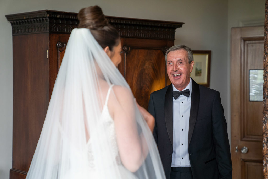 Beaming father of the bride seeing his daughter for the first time in her bridal gown and veil