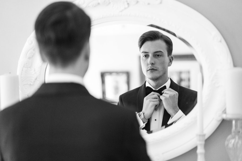 Groom straightening his bow tie in the mirror moments before leaving for the wedding ceremony