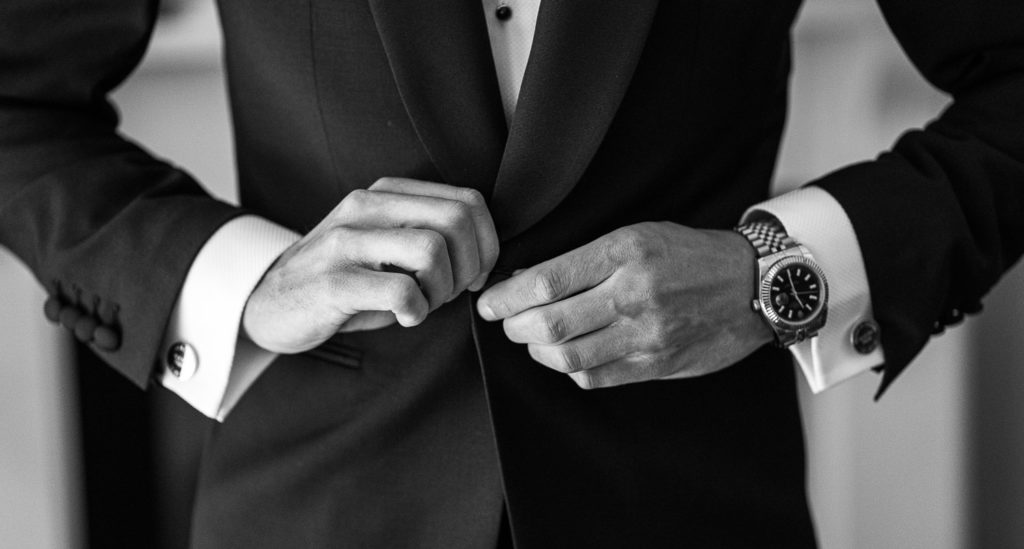 Groom buttoning up his tux as he makes final adjustments
