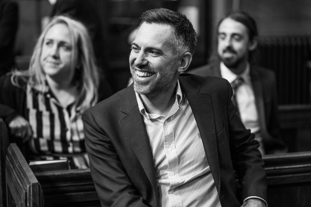 Wedding guest laughing as he sits waiting for the ceremony to begin
