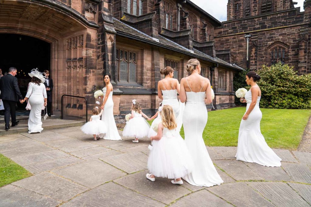 Bridesmaids and flower girls all in white gathering at the entrance of the church just before bride's arrival