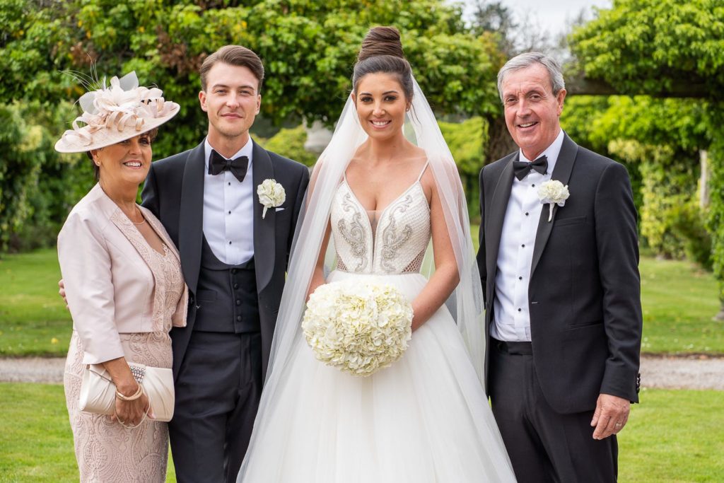 Bride and groom with parents either side in the gardens at Thornton Manor