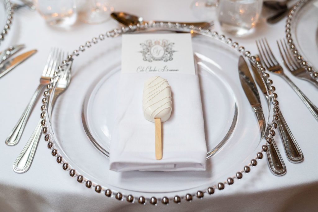 Wedding favour of a white chocolate lolly placed on a napkin sat on a clear wedding breakfast charger