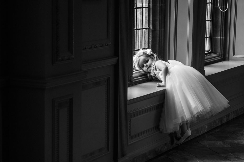Flower girl caught on camera in the moment trying to climb up onto a window seat