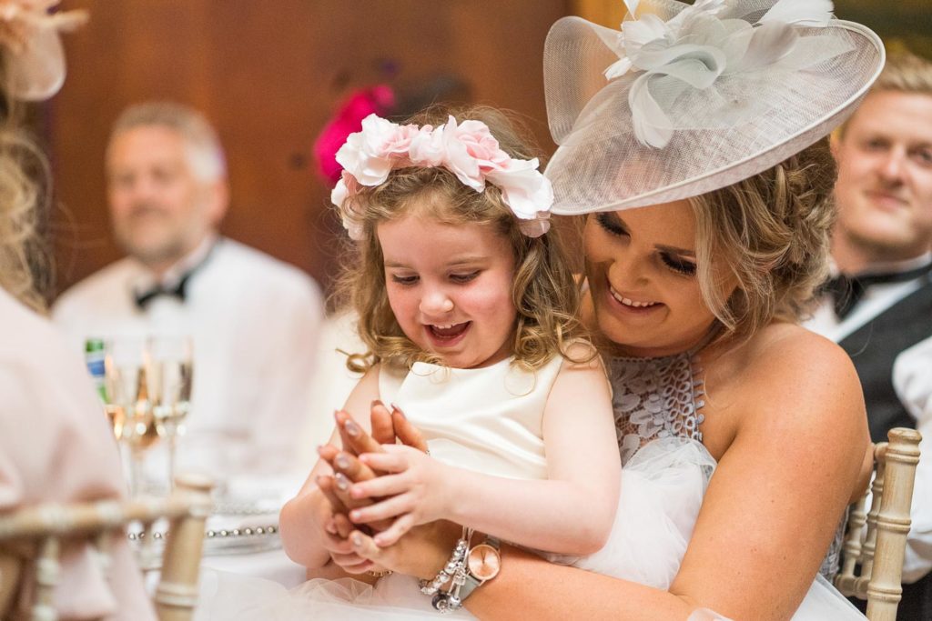 Flower girl sat on her mum's knee clapping and laughing together