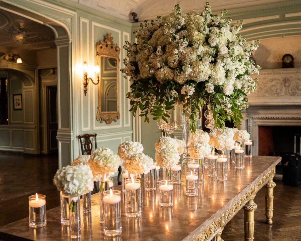 Foyer at Thornton Manor adorned by large table hero of white blossoms and smaller posies in water with candles all around