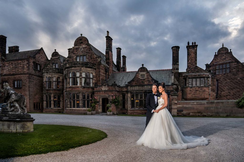 Bride and groom posed in front of Thornton Manor with moody grey clouds overhead