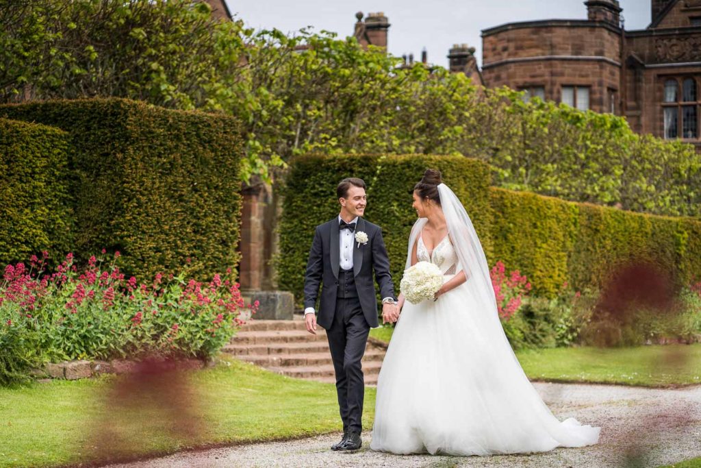 Newlyweds enjoying a relaxing stroll through the gardens smiling and laughing holding hands